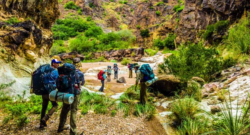 a group of gap year students carrying backpacks hike along a canyon lined greenery on an outward bound semester 